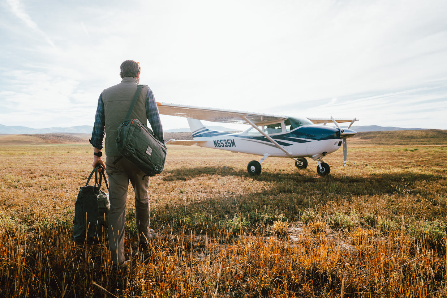 Man with bags walking towards a small airplane in a field
