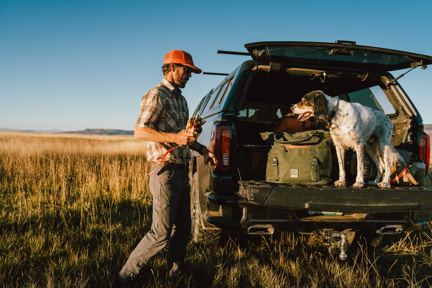 Man with a dog in a field next to an open car trunk